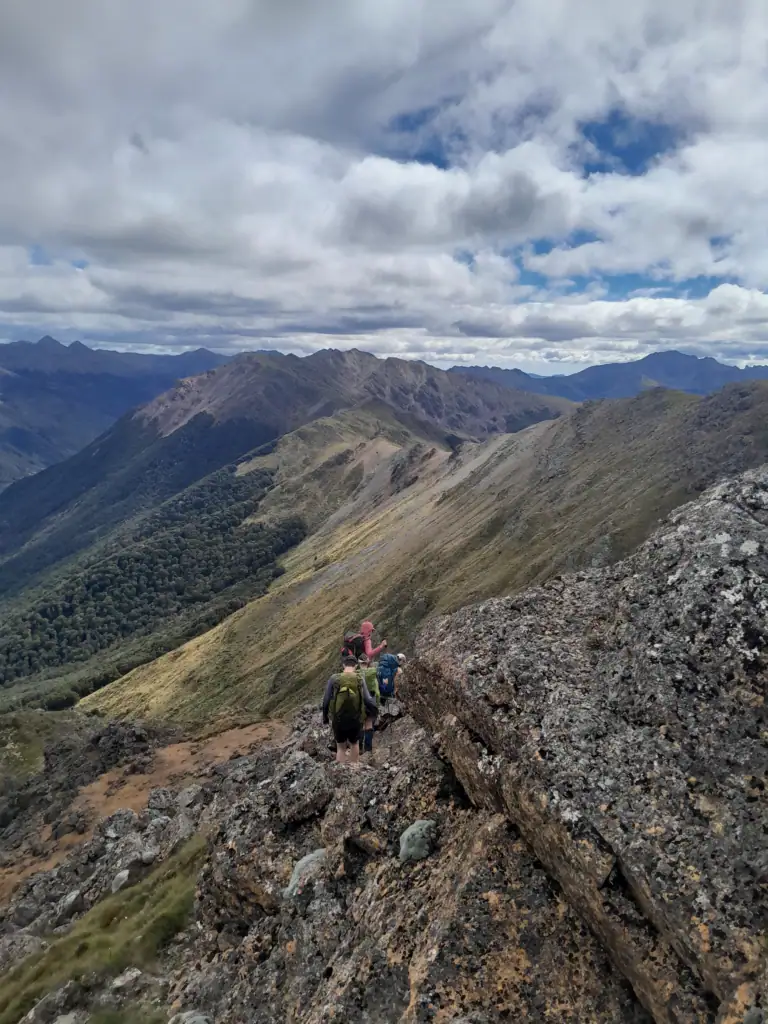 Group of tramping club members negotiating a steep, narrow rocky section of the ridge after Iron Hill on the way to Diamond Lake