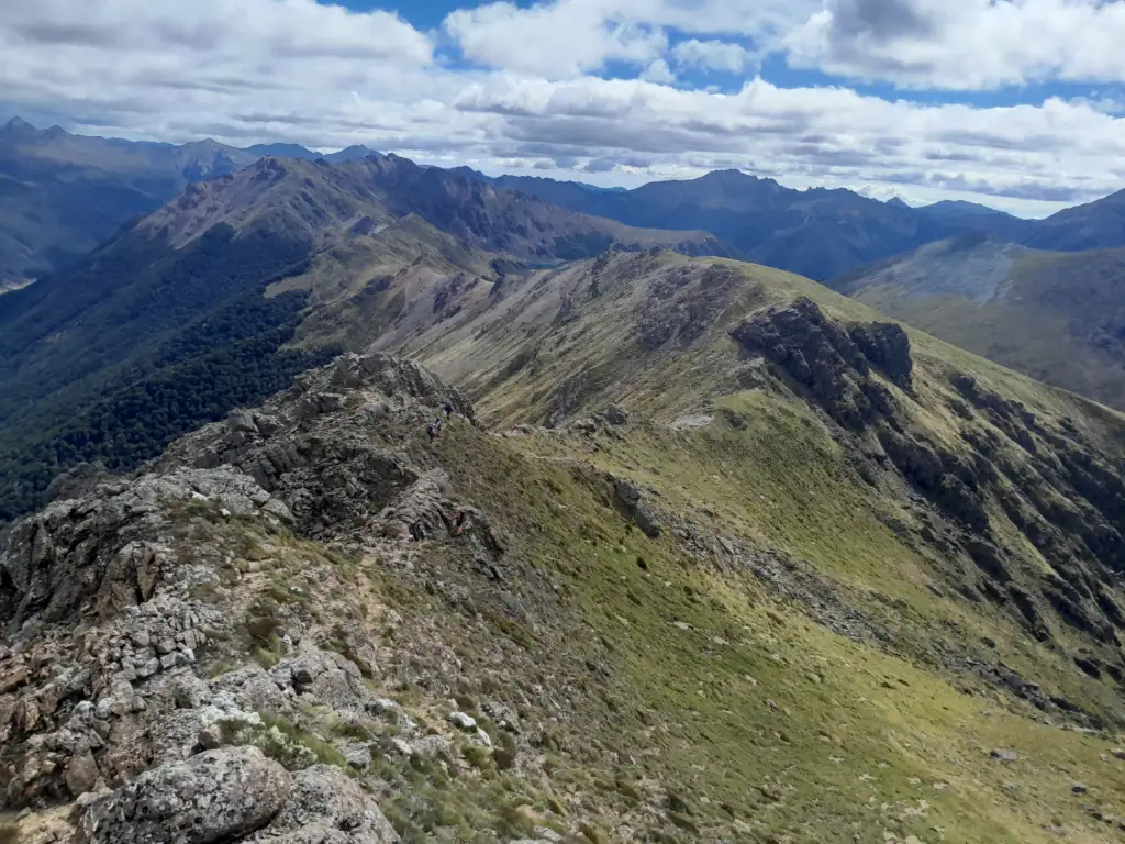 Trampers scrambling along the rocky alpine ridgeline near Point 1631 above Lake Lillie on the Lockett Lakes Loop in Kahurangi National Park.