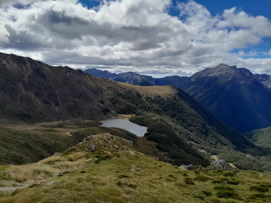 High-altitude view of Ruby Lake nestled in a valley surrounded by bush and tussock along the Lockett Lakes Loop route in Kahurangi National Park.