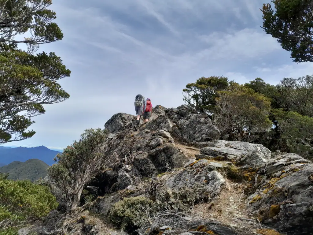 Hikers scrambling across exposed schist rock formations along the ridgeline to Mt Sunday., Richmond Forest park, Marlborough