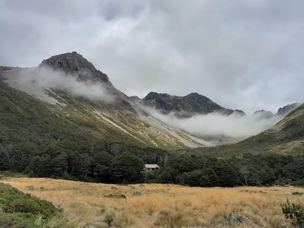 Upper Travers Hut in an open alpine valley surrounded by misty mountains in Nelson Lakes National Park on the Travers-Sabine Circuit. 