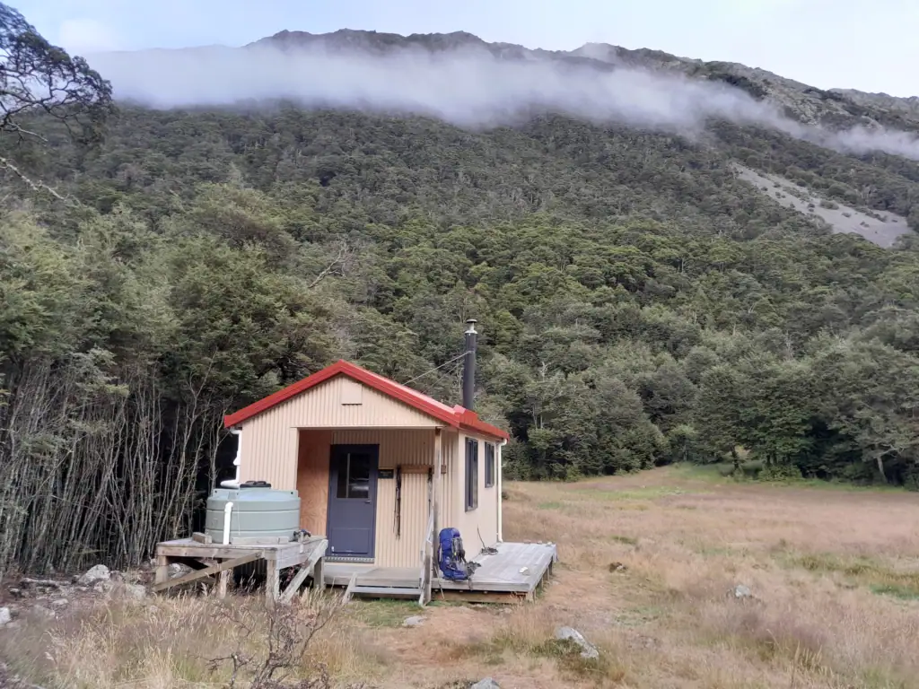 Waiau Hut nestled beneath mist-covered forested hills in St James Conservation Area.