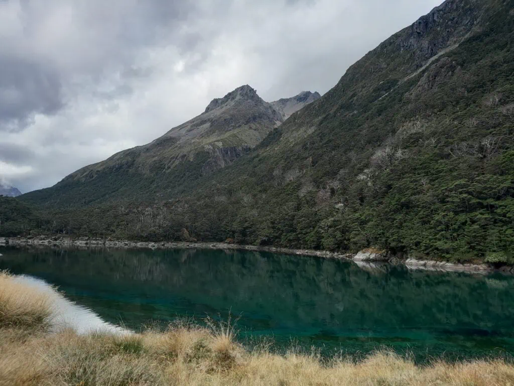 Deep blue and green waters of Lake Rotomairewhenua Blue Lake reflected under mountain peaks on the Waiau pass Route, Nelson Lakes National Park.